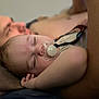 Gunnar is registered to the contest to win money with this photo: baby, pacifier, sleeping, child, adult, blurred_background, rest, comfort, close_up, face, skin, hand, indoor, person, napping, peaceful, couch, relaxation, bonding, infant