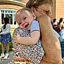 baby, child, hug, smile, happy, person, adult, outdoor, daylight, building, brick_wall, window, dress, patterned_clothing, glasses, hand, grass, side_view, people, nature