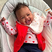 Gianna joined the competition — help win amazing prizes! baby, baby_chair, bib, child, clothing, cushion, cute, happy, heart_pattern, indoors, infant, joyful, navy_pants, person, pink, playful, portrait, red_vest, smiling, toddler