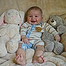 baby, smiling, infant, stuffed_animal, bunny, bear, plush_toy, blanket, cozy, striped_clothing, happy, child, cute, soft_texture, indoors, sitting, portrait, comfort, cuddly, playful