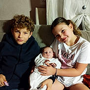 Elyana participe au concours pour gagner de l'argent avec cette photo : child, baby, siblings, couch, indoors, curly_hair, white_clothing, smiling, holding, family, portrait, casual, seated, curtains, radiator, bracelet, light_shadow, tshirt, young, expression
