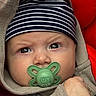 Swann a rejoint le concours — aidez-le/la à gagner de superbes lots ! adorable, baby, beanie, cheek, closeup, clothing, cozy, eyelashes, eyes, face, green_pacifier, hand, hoodie, infant, newborn, pacifier, portrait, red_background, striped_hat, stroller