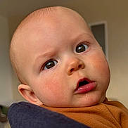 Swann a rejoint le concours — aidez-le/la à gagner de superbes lots ! baby, infant, face, close_up, big_eyes, drool, chubby_cheeks, bald_head, brown_eyes, curious_expression, indoor, portrait, skin, orange_shirt, ear, mouth, eyelashes, high_resolution, candid, person