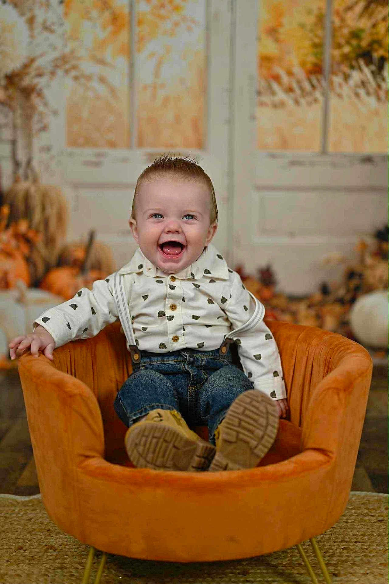 Cannon is registered to the contest to win money with this photo: baby, child, smile, happy, suspenders, jeans, orange_chair, indoor, autumn, pumpkins, background, plush_chair, cute, portrait, sitting, person, floor, shirt, footwear, decor