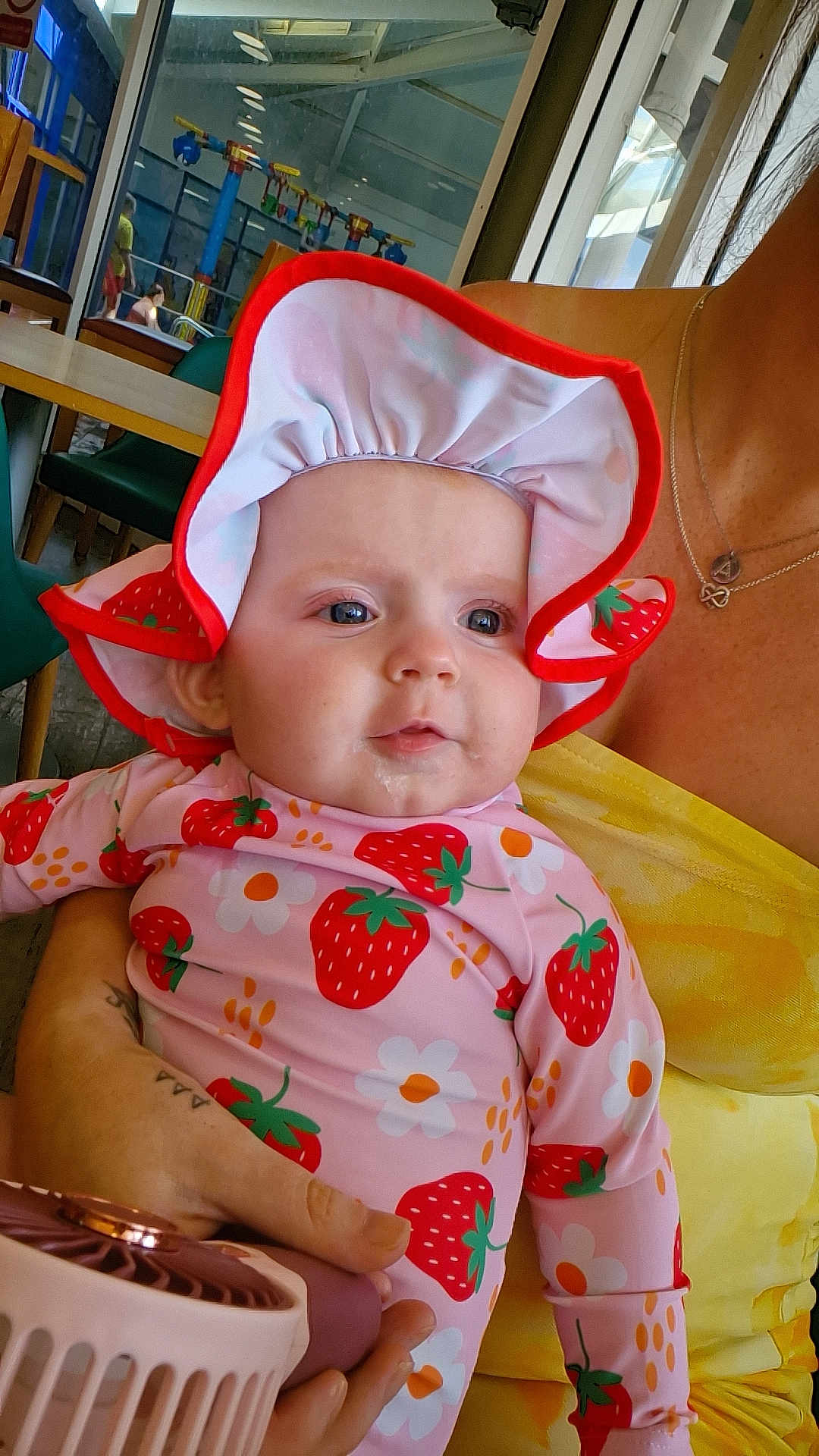 Rosa joined the competition — help win amazing prizes! baby, child, person, infant, hat, strawberry_pattern, flower_pattern, clothing, drool, hand, fan, yellow_top, indoor, table, chair, window, reflection, face, portrait, holding