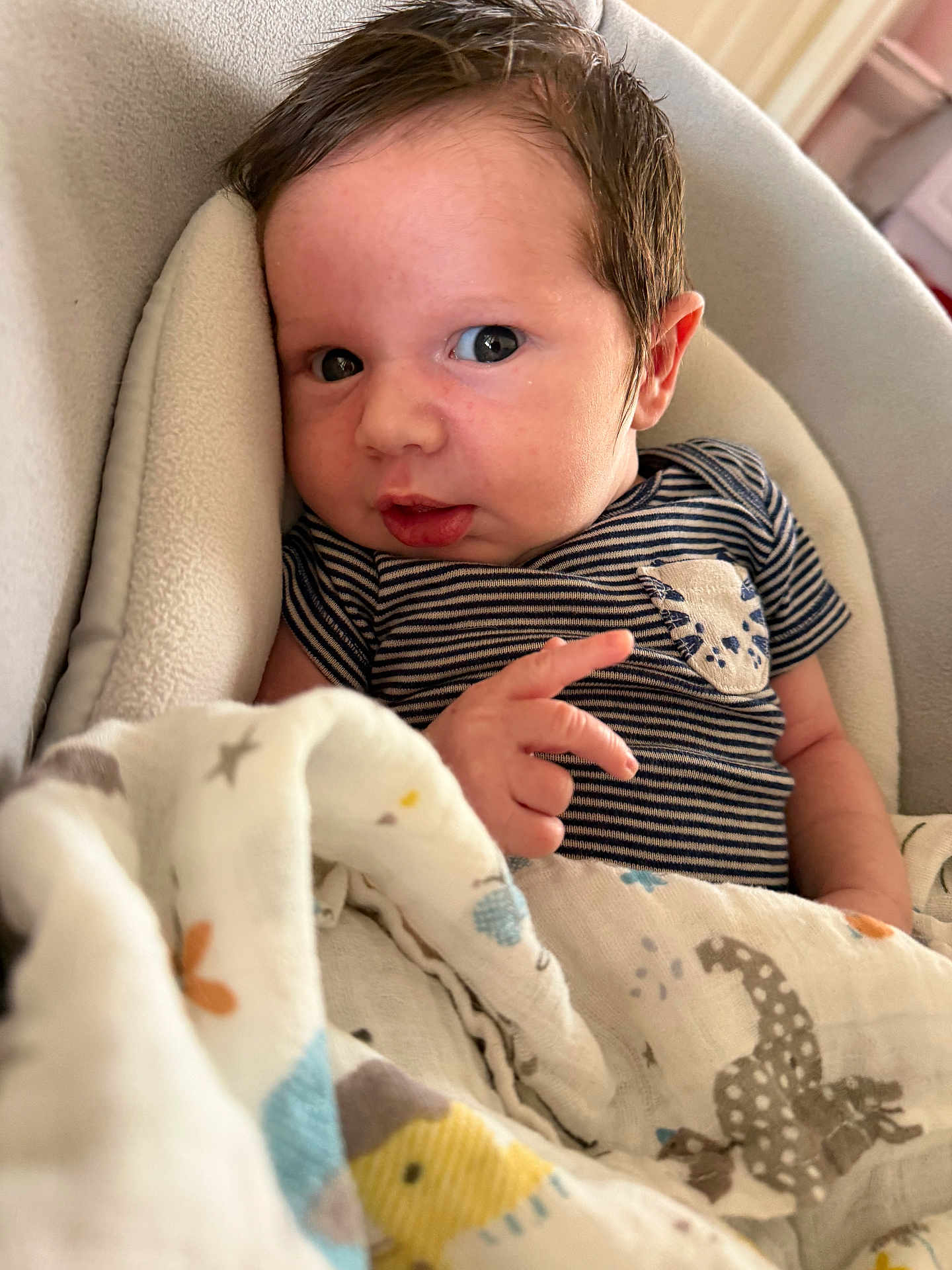 Christopher is registered to the contest to win money with this photo: baby, newborn, infant, face, eyes, hair, hand, onesie, striped_clothing, pocket_detail, blanket, swaddle, patterned_fabric, cushion, portrait, indoors, cozy, soft_texture, skin, ear