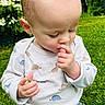 toddler, child, outdoor, grass, greenery, shirt, dinosaur_pattern, hand, thumb_sucking, curious, close_up, nature, baby, long_eyelashes, young_child, casual_clothing, portrait, soft_light, garden, cute