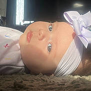 Evie is registered to the contest to win money with this photo: baby, headband, bow, carpet, indoor, child, face, light, sunlight, window, living_room, furniture, floor, clothing, cute, portrait, infant, young_child, home, relaxing