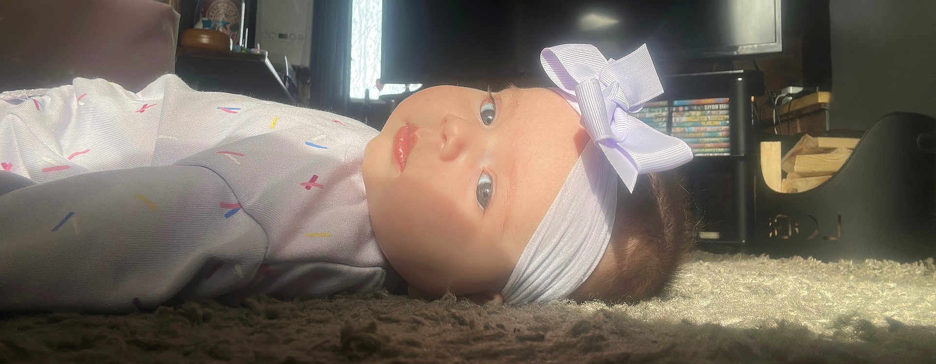 Evie is registered to the contest to win money with this photo: baby, headband, bow, carpet, indoor, child, face, light, sunlight, window, living_room, furniture, floor, clothing, cute, portrait, infant, young_child, home, relaxing