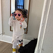 Mia is registered to the contest to win money with this photo: child, toddler, heart_sunglasses, mirror, reflection, mickey_mouse, sweatshirt, pants, sneakers, dog, pet, indoor, hardwood_floor, wall, curtain, posing, playful, portrait, fashion, standing