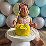 child, baby, toddler, cake, smash_cake, birthday, balloons, party, crown, wand, frosting, dessert, sitting, wood_floor, cake_stand, pink_dress, messy, celebration, portrait, toes