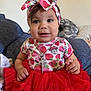 baby, child, girl, red_tutu, headband, strawberry_pattern, minnie_mouse, jewelry, necklace, indoor, couch, pillow, clothing, cute, portrait, smiling, person, sitting, infant, headwear