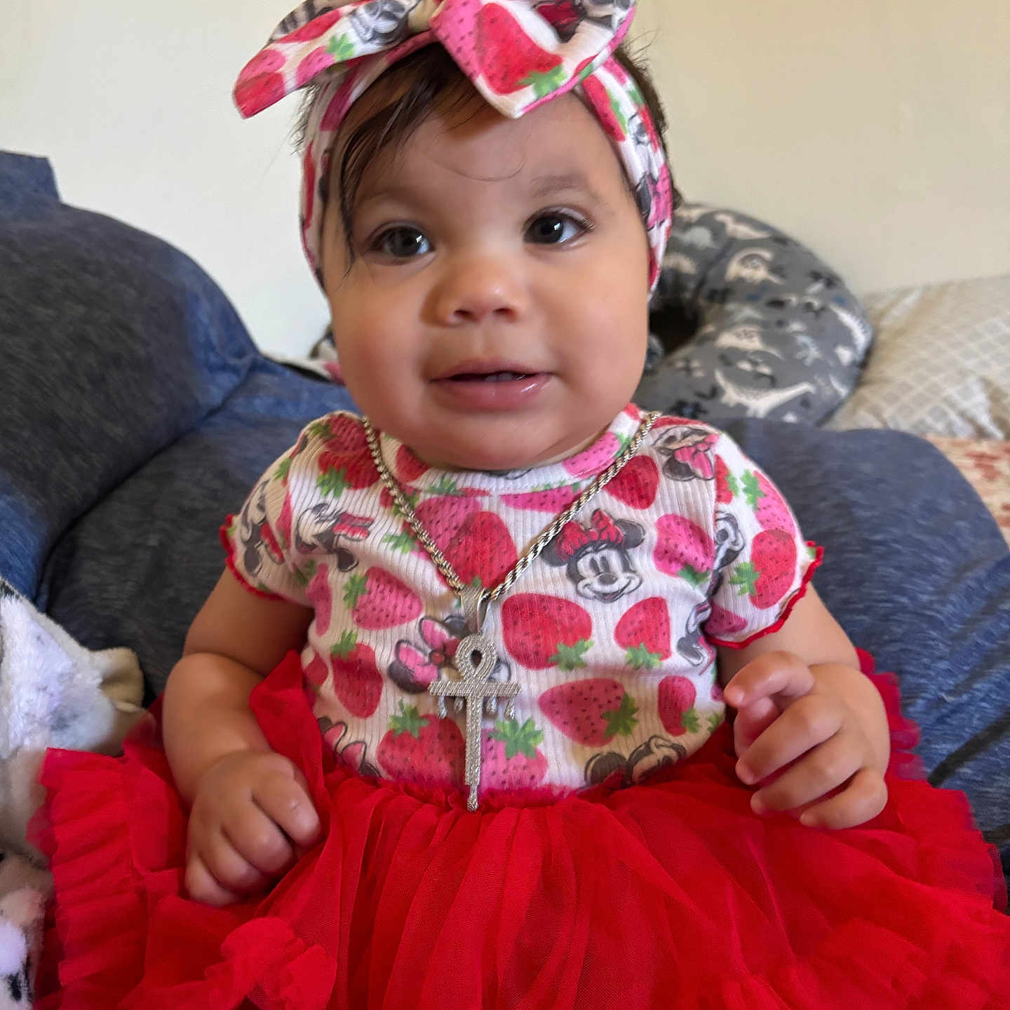 Adina is registered to the contest to win money with this photo: baby, child, clothing, couch, cute, girl, headband, headwear, indoor, infant, jewelry, minnie_mouse, necklace, person, pillow, portrait, red_tutu, sitting, smiling, strawberry_pattern