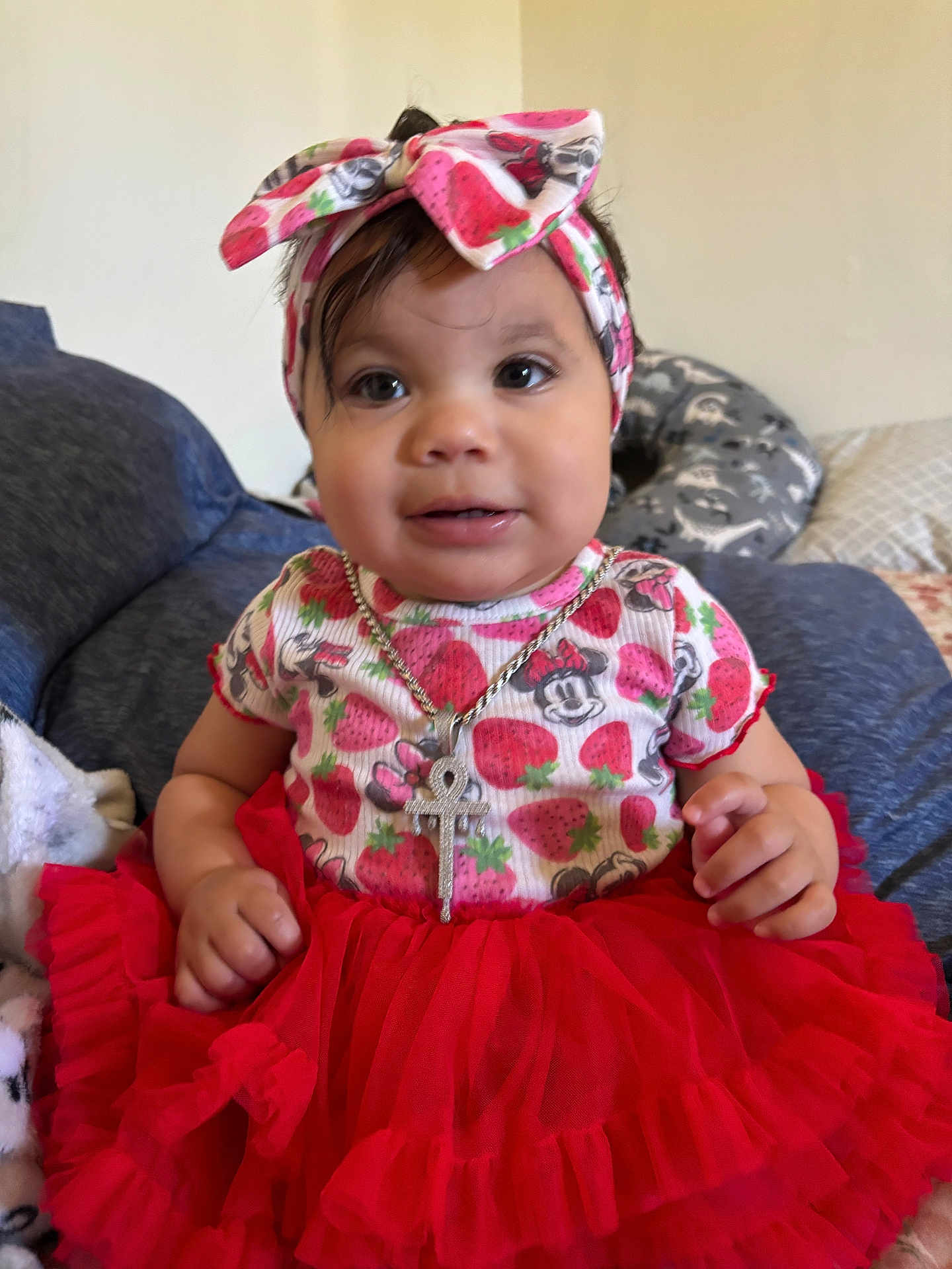 Adina is registered to the contest to win money with this photo: baby, child, girl, red_tutu, headband, strawberry_pattern, minnie_mouse, jewelry, necklace, indoor, couch, pillow, clothing, cute, portrait, smiling, person, sitting, infant, headwear