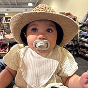 Adina joined the competition — help win amazing prizes! baby, hat, pacifier, indoor, child, curious, white_clothing, sitting, wide_eyes, infant, person, store, shelves, boxes, cute, portrait, face, headwear, young_child, casual