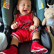 Julian joined the competition — help win amazing prizes! baby, child, infant, smiling, laughing, car_seat, teddy_bear, red_outfit, basketball_jersey, sneakers, shoes, portrait, indoor, seated, happy, toy, vehicle, face, close_up, playful