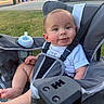 baby, stroller, bottle, outdoor, child, infant, cute, seatbelt, grass, sidewalk, car, trash_bins, sunlight, white_shirt, face, smile, person, legs, hand, parked_vehicle