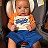baby, child, car_seat, clothing, orange_shirt, blue_shorts, face, eyes, infant, person, seatbelt, sitting, young_child, indoor, cute, portrait, skin, hands, expression, casual
