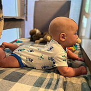 Ronnie is registered to the contest to win money with this photo: baby, infant, onesie, mickey_mouse, lying_down, blanket, checkered, toy, soft_toys, indoor, child, cute, tummy_time, person, head, skin, clothing, bed, resting, young