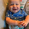 baby, baby_seat, blue_onesie, child, clasped_hands, colorful, cute, face, happy, indoor, infant, monkey_pattern, one_person, playful, portrait, sitting, smiling, sun_pattern, toddler, young_child