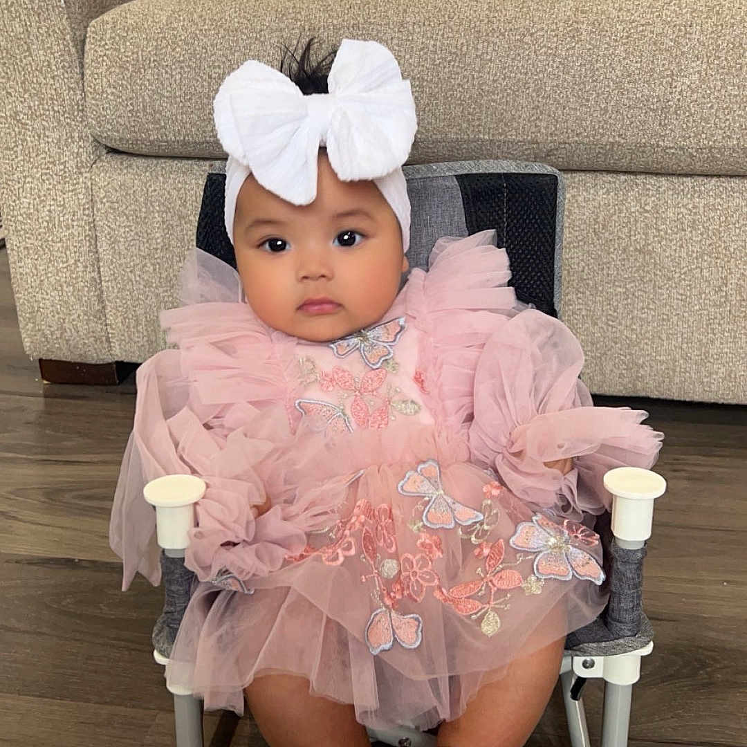 Partha is registered to the contest to win money with this photo: adorable, baby, butterfly_embroidery, chair, child, comfortable, couch, cute, feet, floor, headband, home, indoors, infant, legs, pink_dress, plush, portrait, seated, white_bow