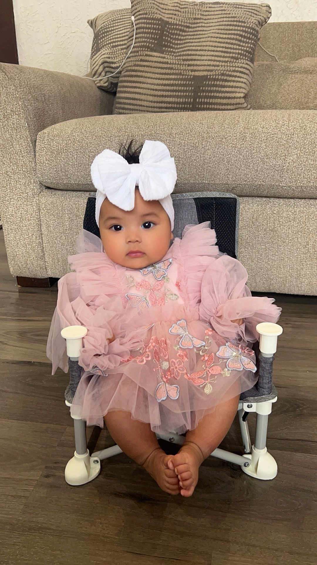 Partha is registered to the contest to win money with this photo: baby, child, pink_dress, white_bow, headband, chair, butterfly_embroidery, cute, indoors, couch, floor, plush, seated, infant, adorable, portrait, legs, feet, home, comfortable