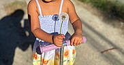 Blossom joined the competition — help win amazing prizes! child, concrete_path, curly_hair, dandelion, dress, flower_pattern, greenery, handlebar, happy, outdoor, person, playful, portrait, scooter, shadow, smiling, standing, sunlight, sunny_day, wall