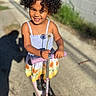 Blossom joined the competition — help win amazing prizes! child, curly_hair, smiling, dandelion, scooter, outdoor, sunlight, dress, flower_pattern, shadow, concrete_path, wall, greenery, happy, playful, sunny_day, person, handlebar, portrait, standing