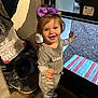 toddler, child, indoor, smiling, purple_bow, gray_outfit, shoes, door, mat, happy, standing, young_child, person, footwear, carpet, floor, toy, clothing, hair_bow, expression