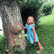 Aliya participe au concours pour gagner de l'argent avec cette photo : child, girl, blue_dress, tree, grass, greenery, outdoor, nature, playful, pose, pucker_lips, sandals, summer, daylight, bushes, trunk, leaf, young, cute, person