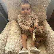 Victor participe au concours pour gagner de l'argent avec cette photo : baby, child, armchair, toy, teddy_bear, giraffe_toy, clothing, suspenders, shorts, shoes, striped_shirt, indoor, furniture, cozy, cute, smile, face, person, sitting, curious