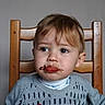 toddler, child, face, chair, sweater, food, messy, red_sauce, chocolate, spoon, table, indoor, portrait, expression, young_child, person, clothing, hair, looking_away, seated
