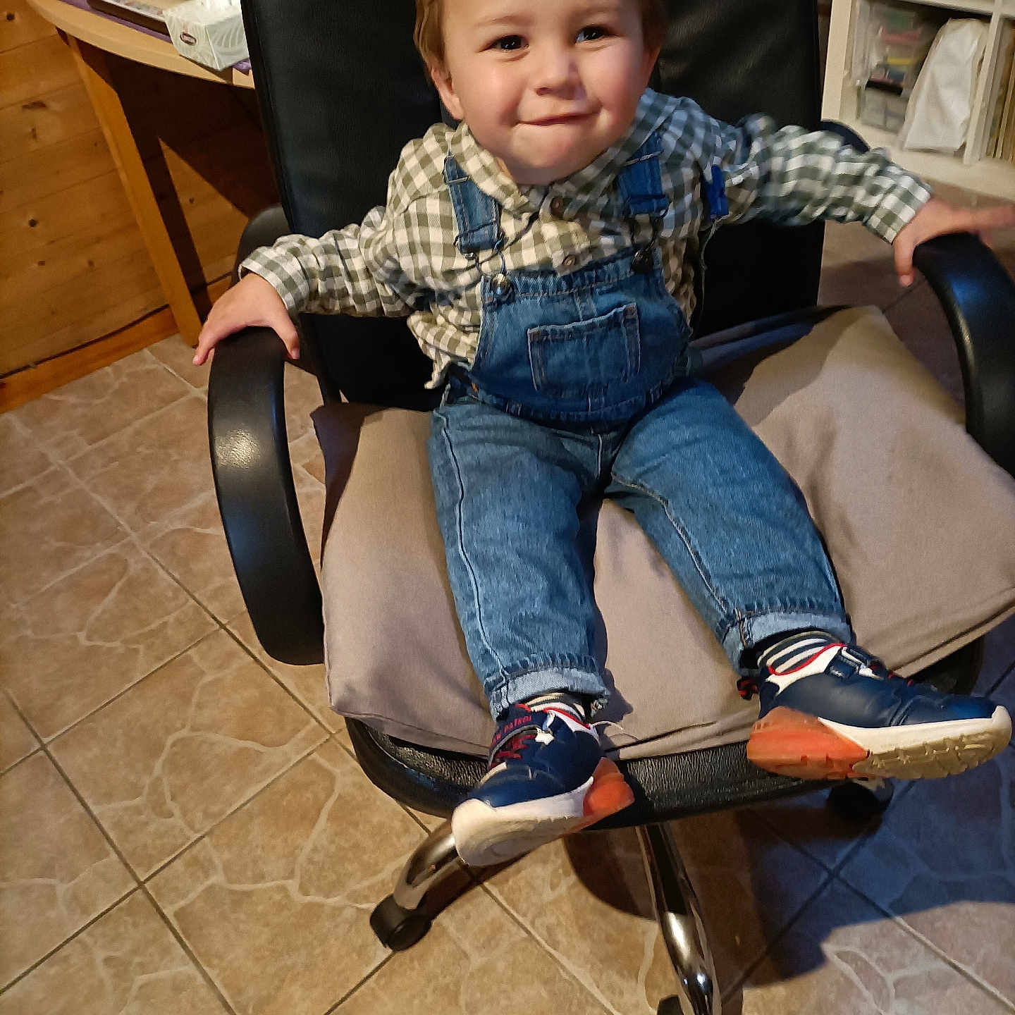 Aaron a rejoint le concours — aidez-le/la à gagner de superbes lots ! toddler, child, smiling, denim_overalls, checkered_shirt, office_chair, indoor, tile_floor, wooden_furniture, casual_clothing, sneakers, happy, cute, young_child, person, seated, home_interior, playful, small_child, portrait