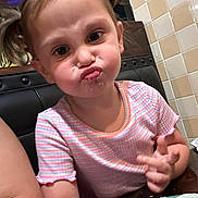 Gracelyn is registered to the contest to win money with this photo: child, toddler, face, pigtails, pink_shirt, striped_clothing, table, plate, food, restaurant, tile_wall, person, pout, cute, indoor, portrait, expression, seated, dining, funny_face