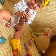 Sailey participe au concours pour gagner de l'argent avec cette photo : baby, child, yellow_headband, yellow_socks, chocolate_bunny, foil_wrapped_chocolate, plush_bunny, beige_blanket, smiling, sitting, indoors, cute, easter, toy, soft_toy, holiday, festive, happy, portrait, person