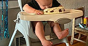 Waylon is registered to the contest to win money with this photo: baby, birthday, birthday_cake, cake_smash, high_chair, eating, food, frosting, celebration, balloons, streamers, indoor, home, wood_floor, infant, black_shirt, bare_feet, party, portrait, funny