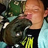Neo is registered to the contest to win money with this photo: affection, black_dog, blanket, bond, casual_clothing, close_up, comfort, cozy, cute, dog, face, friendship, home, indoor, kiss, person, pet, pillow, relaxation, smile