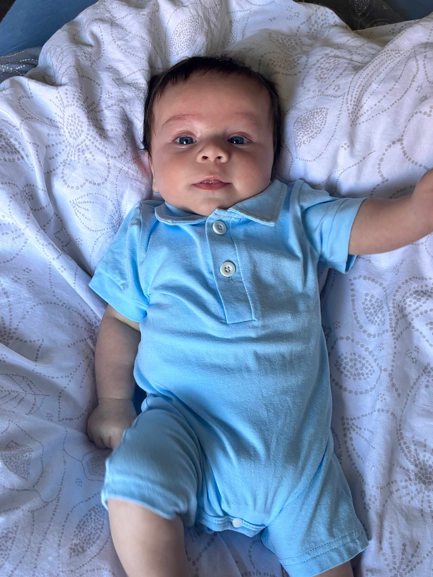Ezio participe au concours pour gagner de l'argent avec cette photo : baby, infant, blue_onesie, blanket, patterned_blanket, lying_down, face, eyes, cheeks, smile, arm, leg, skin, cute, child, young, indoors, soft_light, portrait, clothing
