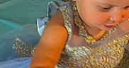 Emery is registered to the contest to win money with this photo: background, blue, bow, bubbles, celebration, child, costume, curious, dress, earrings, face, girl, gold, hair, hand, indoor, portrait, seashells, sparkles, toddler