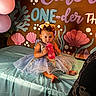 Emery is registered to the contest to win money with this photo: baby, background, balloons, birthday, blue, celebration, child, decorations, dress, event, face, gold, indoor, party, person, pink, sippy_cup, smile, table, toddler