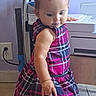Emery is registered to the contest to win money with this photo: toddler, child, plaid_dress, pink, blue, indoor, floor_tiles, curious, person, baby, short_hair, home, cabinet, hand, standing, wall_outlet, appliance, candid, portrait, expression
