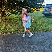 Rosaley is registered to the contest to win money with this photo: child, girl, backpack, pink_bow, pink_hair, tree, grass, driveway, sidewalk, toy, car, jeep, outdoor, sunlight, casual_clothing, sneakers, playful, nature, summer, portrait