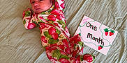 Haysley joined the competition — help win amazing prizes! baby, infant, onesie, red_bow, strawberry_pattern, blanket, green_blanket, sign, handwritten_sign, milestone, one_month, cute, lying_down, headband, newborn, celebration, person, face, soft_texture, indoors
