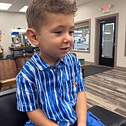 Kacey joined the competition — help win amazing prizes! child, boy, curly_hair, blue_shirt, striped_shirt, blue_shorts, sitting, indoor, barbershop, salon, chair, mirror, ceiling_lights, waiting, portrait, casual_clothing, young, cute, person, haircut