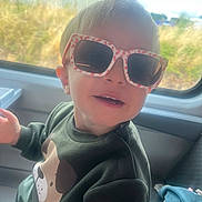 Sam participe au concours pour gagner de l'argent avec cette photo : toddler, child, sunglasses, smile, green_sweater, dog_print, window, vehicle_interior, seat, playful, blond_hair, casual_clothing, indoor, daylight, portrait, cute, happy, fun, young_child, closeup