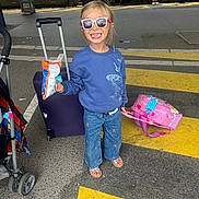Eloïse a rejoint le concours — aidez-le/la à gagner de superbes lots ! child, girl, sunglasses, blue_sweatshirt, butterfly, jeans, sandals, luggage, pink_suitcase, train_station, train, platform, snack, smile, travel, waiting, outdoor, daylight, road_markings, stroller