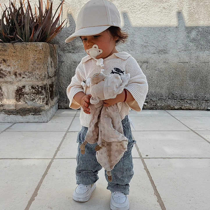 Juliann a rejoint le concours — aidez-le/la à gagner de superbes lots ! toddler, child, pacifier, plush_toy, cap, striped_pants, white_shoes, outdoor, plant, potted_plant, wall, tile_floor, cute, standing, young_child, clothing, casual, innocence, daylight, portrait