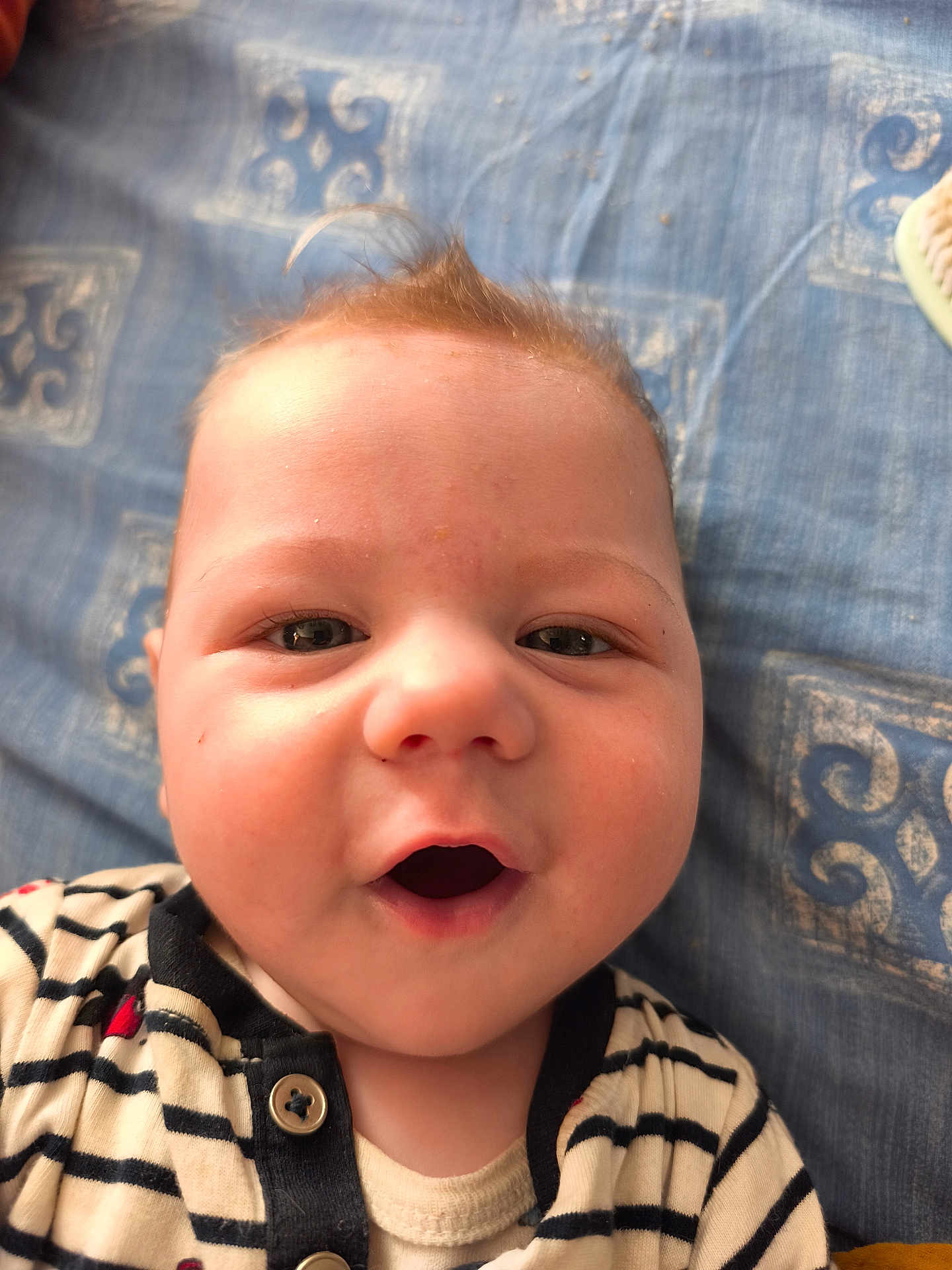 Mélicio a rejoint le concours — aidez-le/la à gagner de superbes lots ! baby, infant, face, close_up, striped_clothing, cute, child, smiling, happy, portrait, young_child, lying_down, patterned_blanket, skin, eyes, mouth_open, buttoned_shirt, indoors, head, person