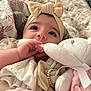baby, infant, bow_headband, blanket, stuffed_animal, plush_toy, hand, face, eyes, long_eyelashes, pacifier, bedding, soft_toy, cute, portrait, indoors, clothing, accessory, gaze_up, cozy