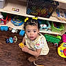 Amber is registered to the contest to win money with this photo: toddler, child, toy, yellow_bow, dress, brown_boots, wooden_floor, shelf, plastic_toys, block, stuffed_animal, indoor, playroom, curly_hair, person, cute, looking_up, colorful, floor, young_child